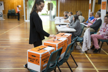 A woman in a school hall on election day, putting her voting paper in a ballot box.