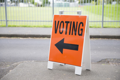 Orange sign that says ‘voting’, with an arrow pointing left, on the side of a street.